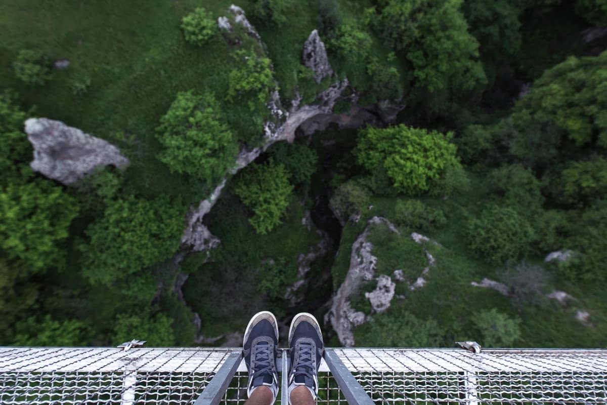 A person standing at an uncertain edge, paused before a step they cannot fully see — the physical weight of faith before the outcome is visible.