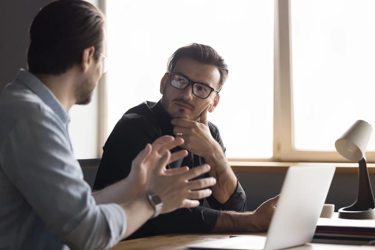 Two colleagues in conversation, one listening intently — the posture of someone learning rather than instructing.