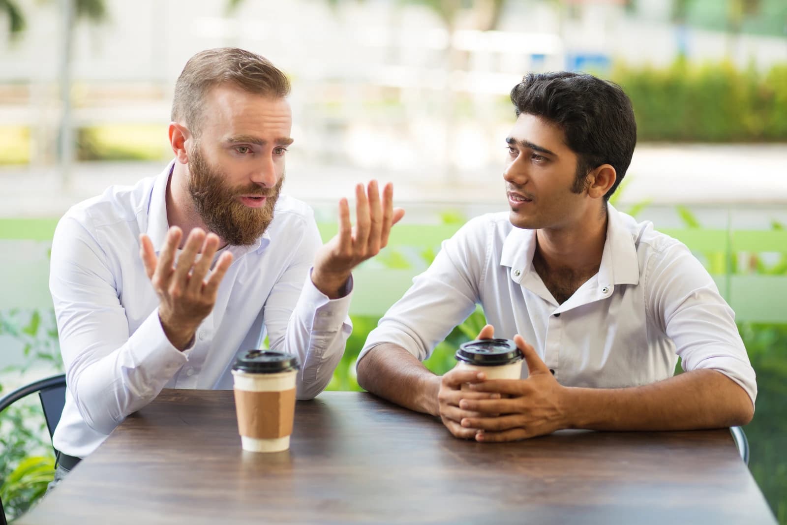 Two people seated across from each other at a café table, mid-conversation, one listening without rush.